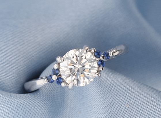 Round diamond engagement ring accented by blue stone