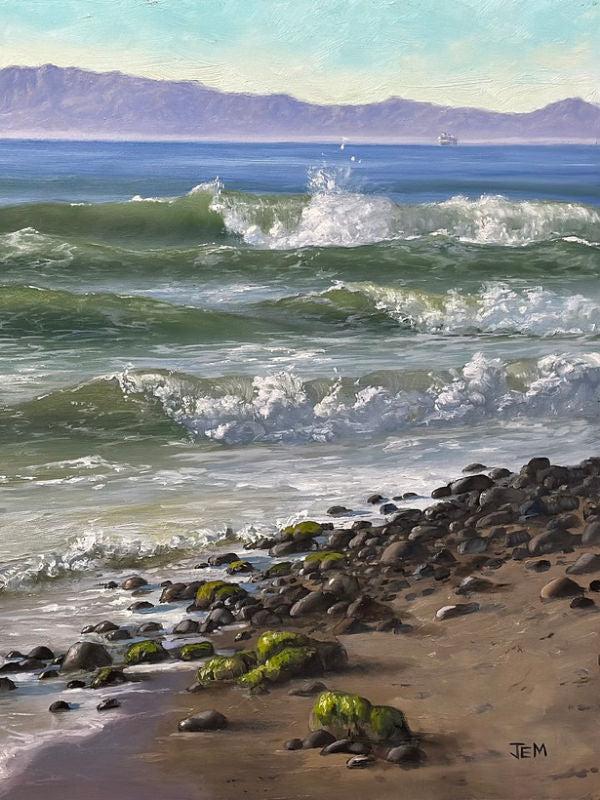 A painted coastal seascape showing green and white ocean waves rolling onto a rocky beach, with distant blue mountains and a pale sky. The Paddle Out by Jem Atwater