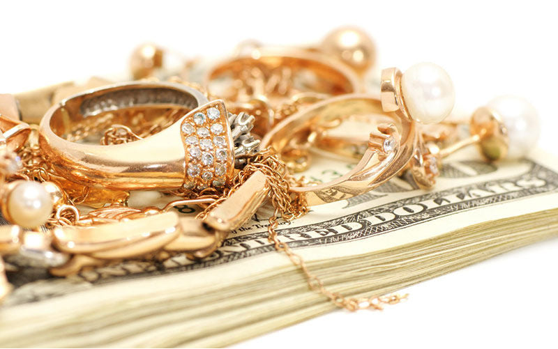 Gold jewelry including rings and a necklace on top of U.S. dollar bills.