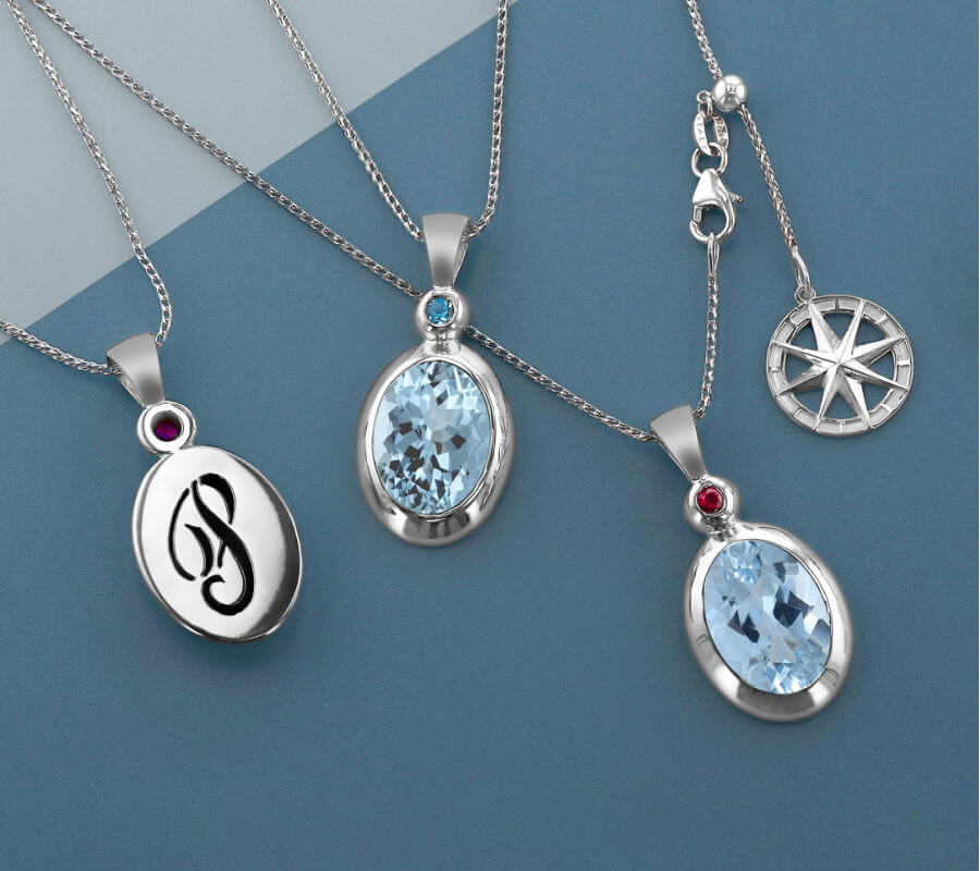 Oval Aquamarine pendants with varying gemstones accenting each, with a "P" inscribed on the back and a compass dangle.