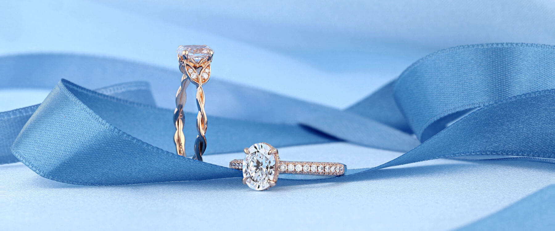 Two diamond engagement rings shown off with a blue ribbon
