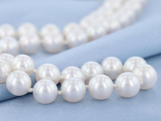 Akoya pearl strand with knots between each pearl on a blue fabric background