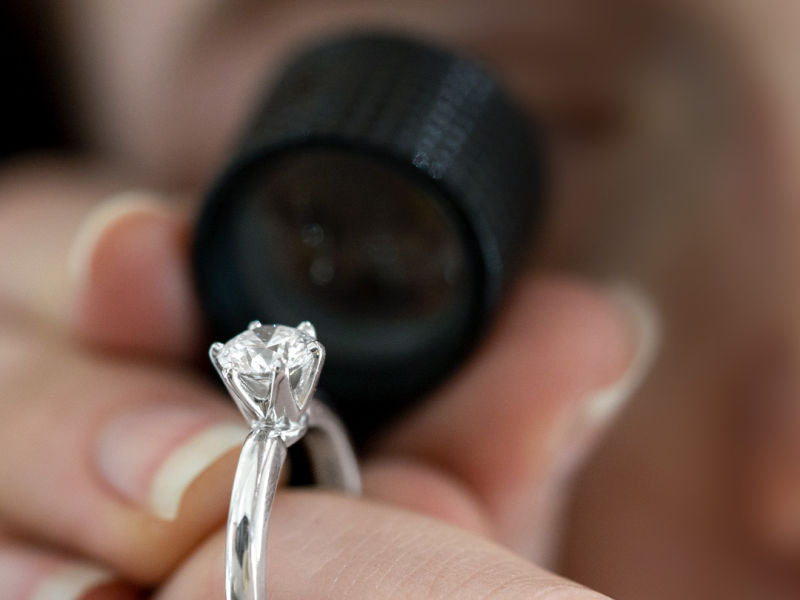Diamond solitaire engagement ring being looked at with a loupe
